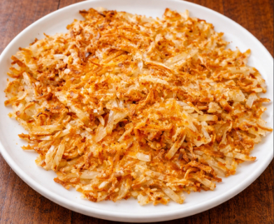 Golden hash browns on a white plate, on a wooden table.